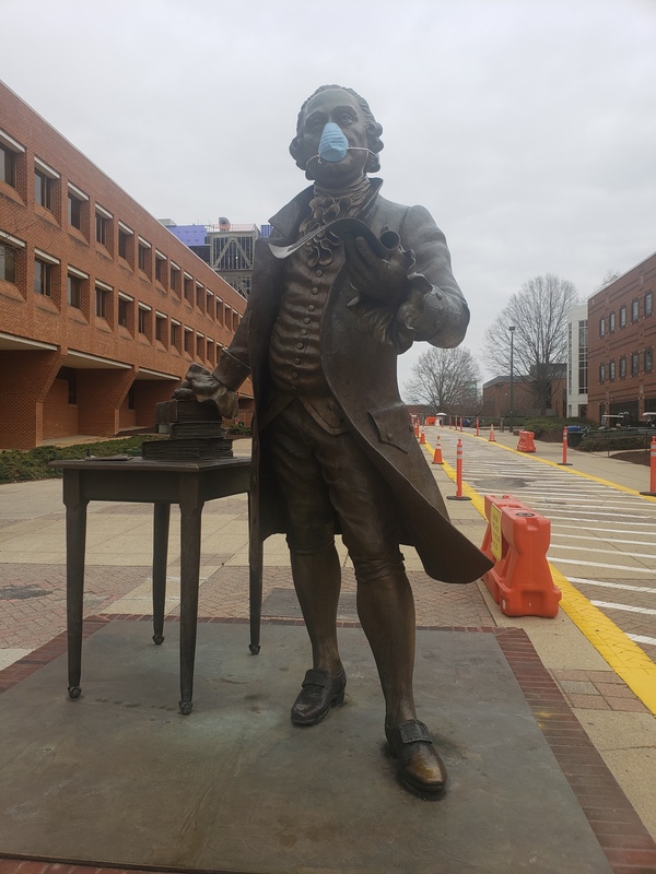 A bronze George Mason statue poses with a blue surgical mask on his face. 