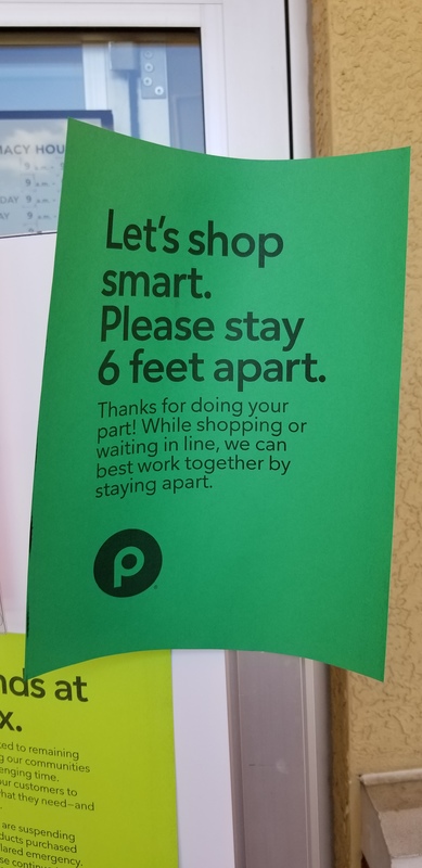 A green paper sign in a grocery store telling its patrons about keeping six feet away from other customers and to practice social distancing. 