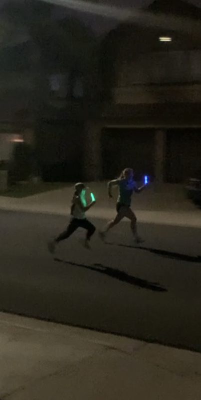 This is a blurry picture taken of two people running down a residential street at night holding glow sticks. 
