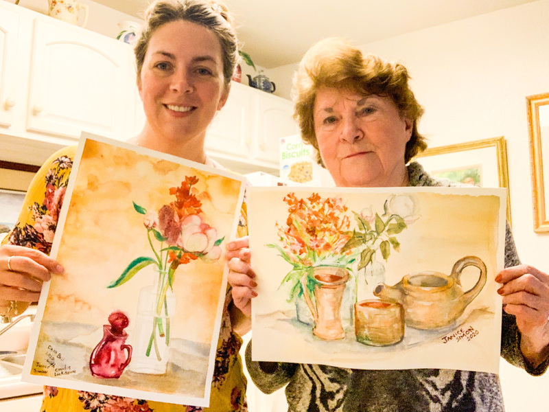 Image of two women holding their paintings of a vase of flowers.