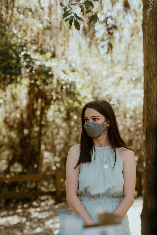 This is a picture of a woman dressed in formal attire standing outside. She is wearing a face mask. 