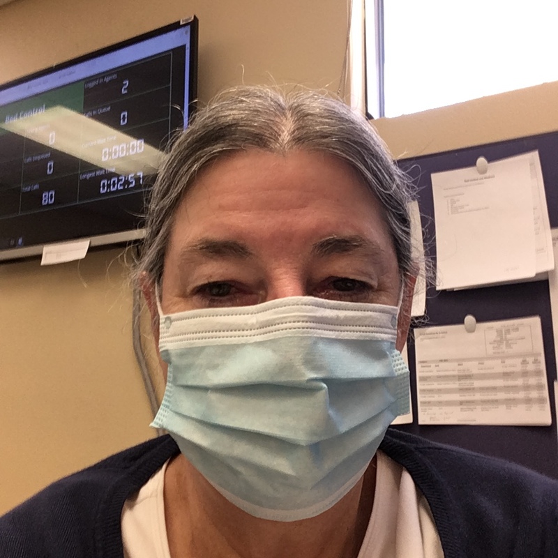 This is a picture of a woman wearing a face mask while looking tiredly at the camera. 
