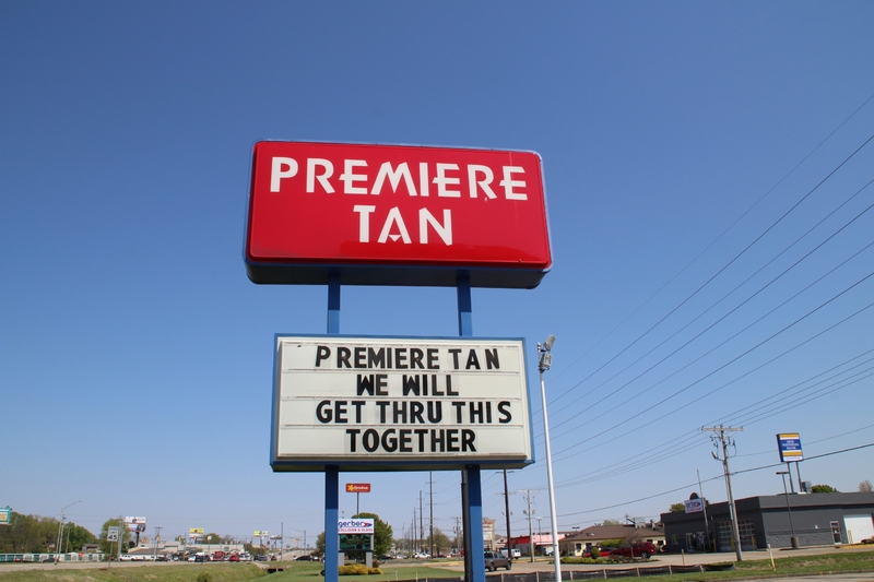 A business sign reading "Premiere Tan, We Will Get Thru This Together". 