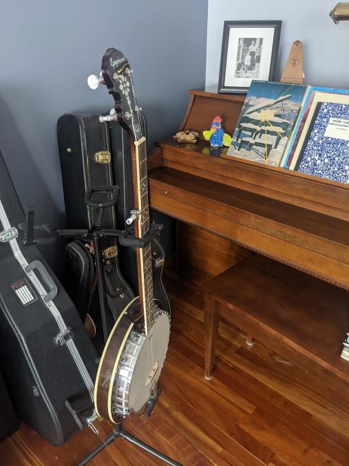 Banjo on a stand next to a wooden, upright piano.