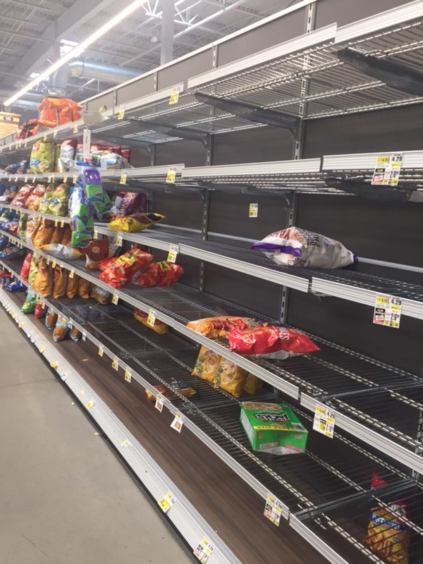 An aisle in a grocery store that has barely stocked bags of chips on the shelves. 
