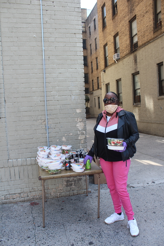 Image of a woman in a mask who's standing next to a table of food she's ready to hand out.