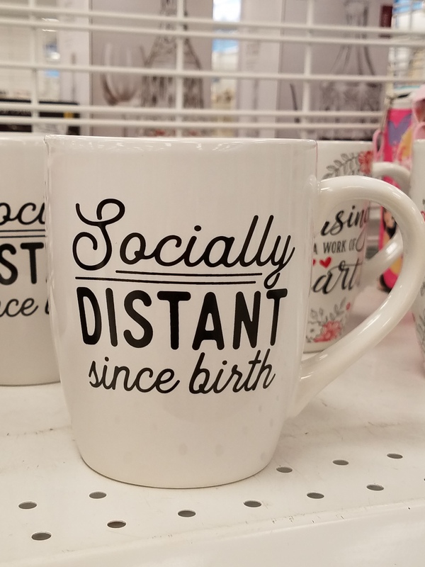 This is a picture of a coffee mug which has the message "Socially distant since birth" written in cursive on it. 