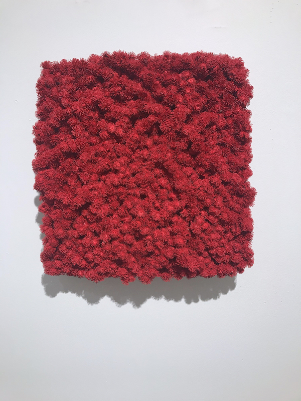 This is a picture of a square mass of bight red, fluffy, stringy material that is hanging on a wall.