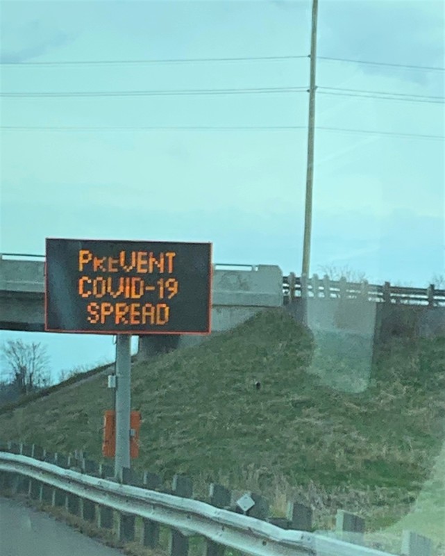 Image of a sign on the side of the highway which reads prevent Covid-19 spread.