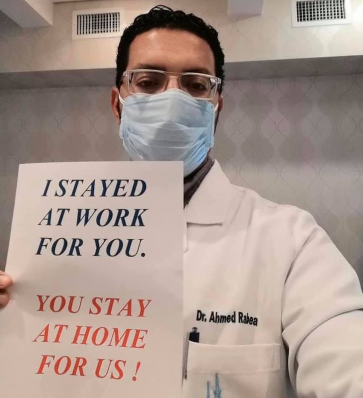 Image of a male doctor holding a sign which reads I stayed at work for you, you stay at home for us.