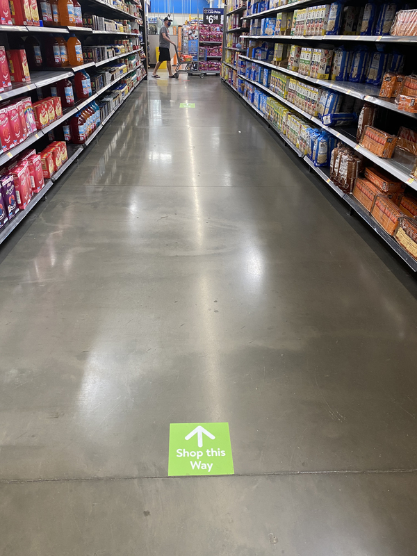 A sign on the floor indicting which way to travel down an aisle at a grocery store.