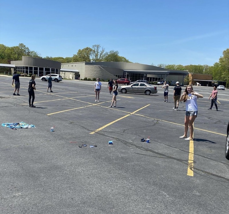 Eleven teenagers scattered around the parking lot of their High School, practicing social distancing during the pandemic. 
