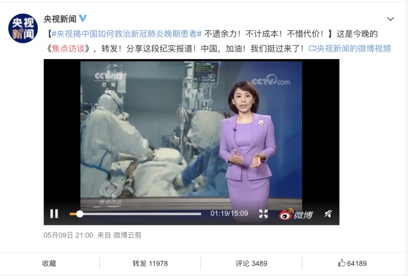 Screenshot of a Chinese news broadcast. A woman news anchor in a purple suit is standing in front of a photo of medical personnel in a hospital helping a patient. 