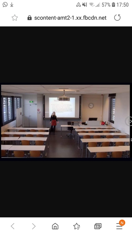A screenshot of a teacher standing in front of a pulled down projector screen in an empty classroom.