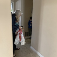 This is a picture of a woman carrying several shopping bags stopped in a hallway. She is trying to talk to a young buy who is wearing a face mask and shrinking away from her as if he is afraid. 
