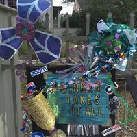 This is a picture taken of a person's fence, which has been decorated with multiple graphics relating to viral memes that were popular during the pandemic. A blue and black sign reads "winner takes all", with many brightly colored decorations covering the fence. 