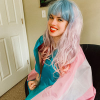 a woman wrapped in a trans pride flag and dyed pink and blue hair