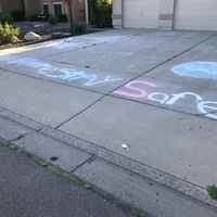 The words "Stay home, stay safe" are written with chalk on a driveway. 