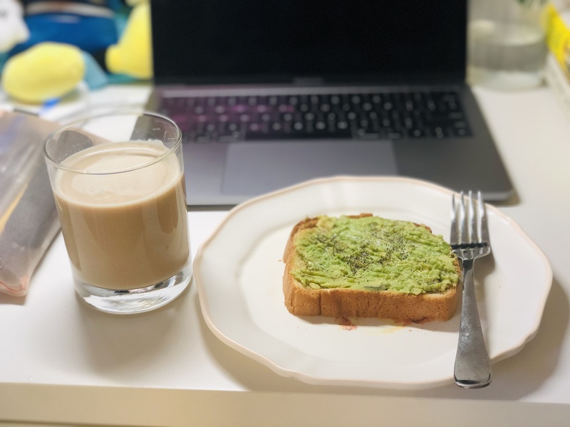 A plate with avocado toast with a glass of coffee to the left of it. In front of the plate is a laptop.