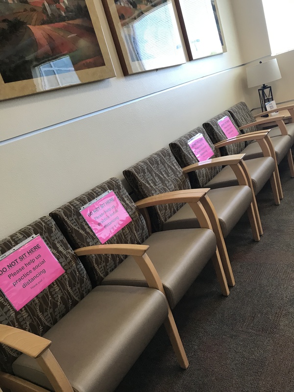 Chairs in a medical waiting room with signs reading Do Not Sit Here, please help us practice social distancing.
