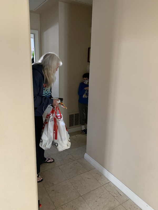 This is a picture of a woman carrying several shopping bags stopped in a hallway. She is trying to talk to a young buy who is wearing a face mask and shrinking away from her as if he is afraid.