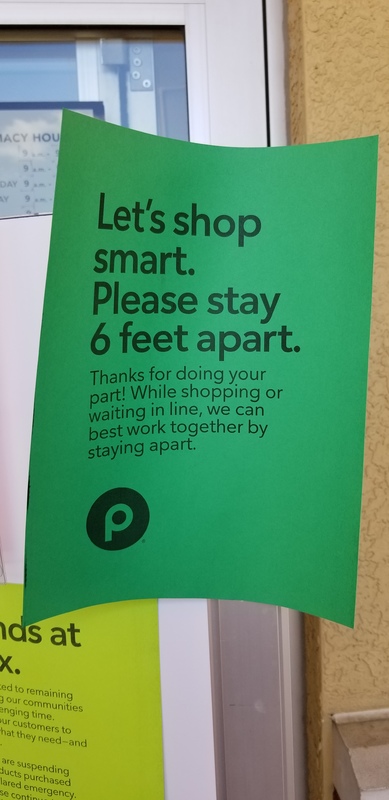 A green paper sign in a grocery store telling its patrons about keeping six feet away from other customers and to practice social distancing.