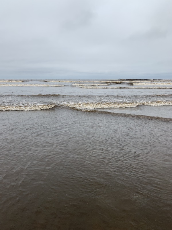 Waves rolling in at the beach under a grey sky.
