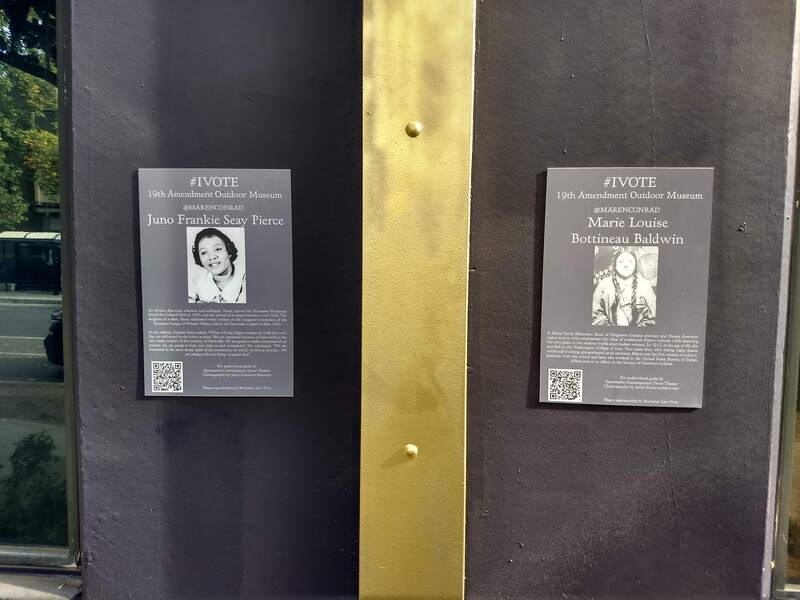 This is a picture of two plaques, which inform the reader of the identity of some of the women depicted in the 19th Amendment Outdoor Museum murals nearby. One reads: "Juno Frankie Seay Pierce", and the other reads: "Marie Lousie Bottineau Baldwin".