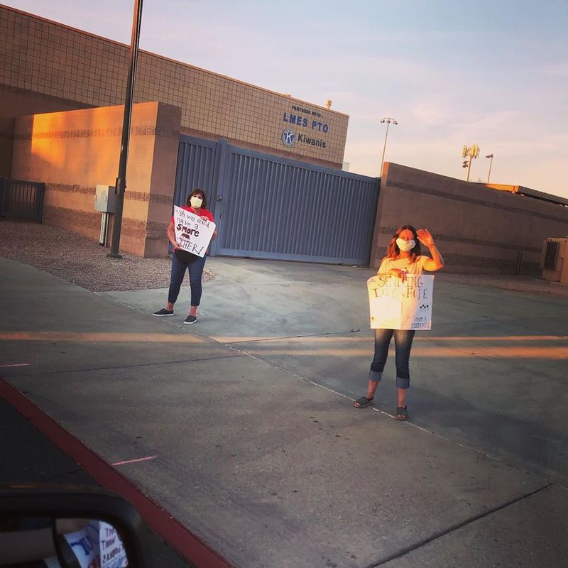 Two teachers holding signs outside of school.