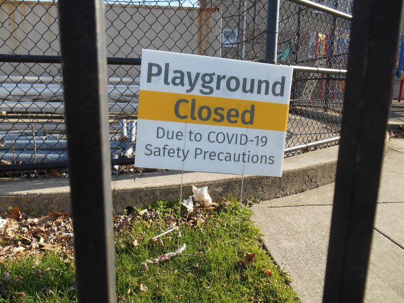 A yard sign that says: "Playground Closed Due to COVID-19 Safety Precautions".