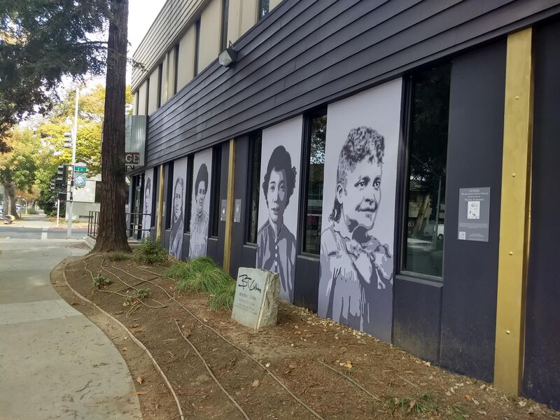 This is a picture taken of a series of murals that are painted on the side of a building. Various women in different periods of clothing are depicted in black and white.