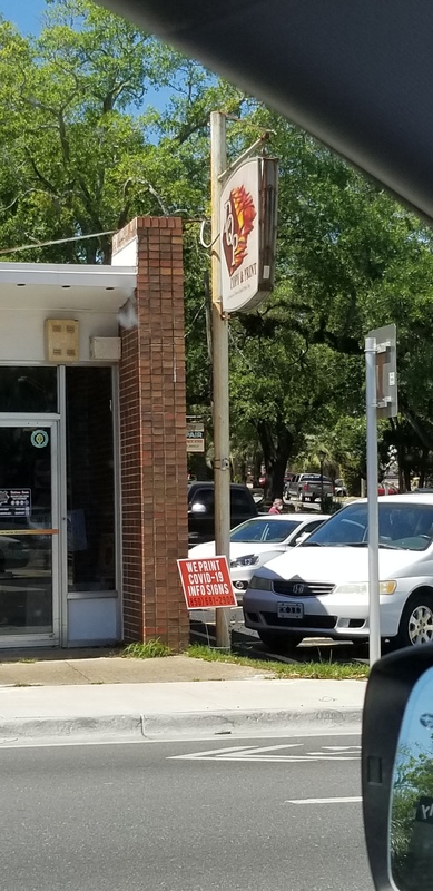 The front of a business that makes information signs. In the yard to right in front of the door has a sign that says: "We print COVID-19 info signs".