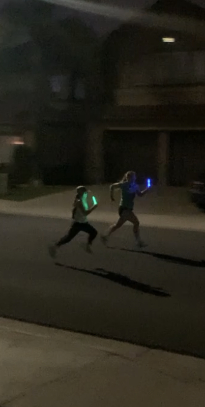 This is a blurry picture taken of two people running down a residential street at night holding glow sticks.