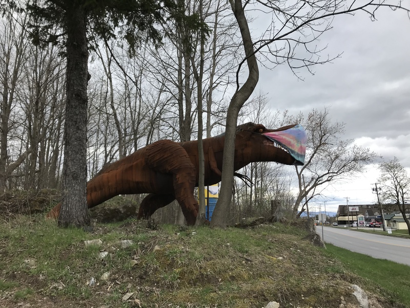 A statue of a dinosaur with a mask on in the woods.