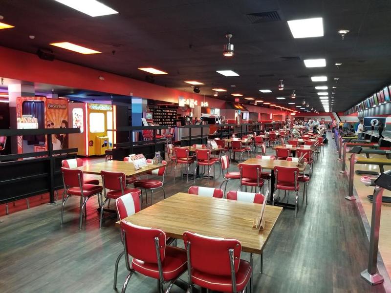 A bowling alley with empty red and white tables and chairs going off into the distance.
