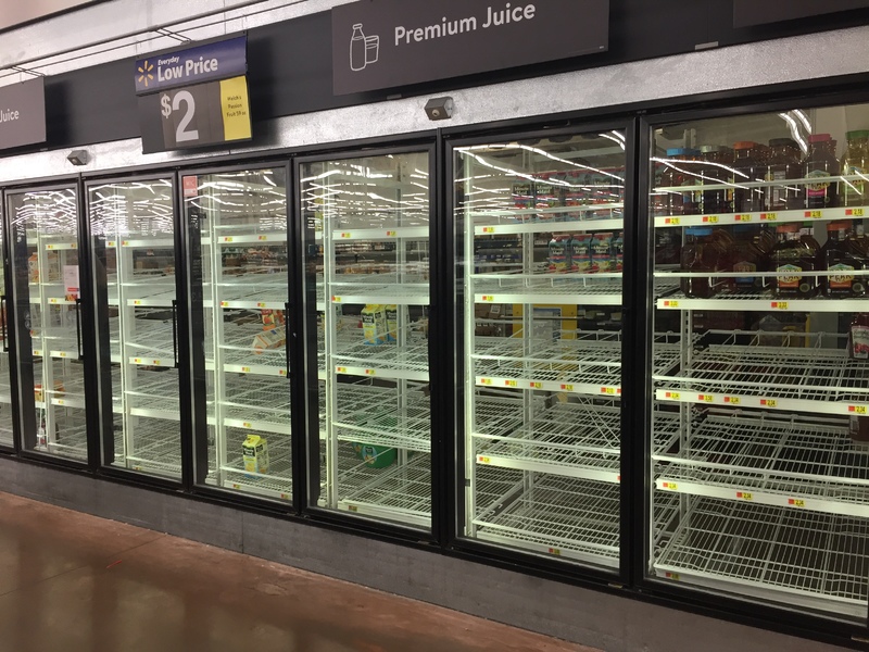 Rows of empty glass refrigerators in a grocery store with a sign that says Premium Juice above.