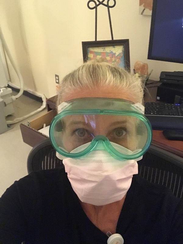 A woman working at a medical center wearing goggles and two masks.