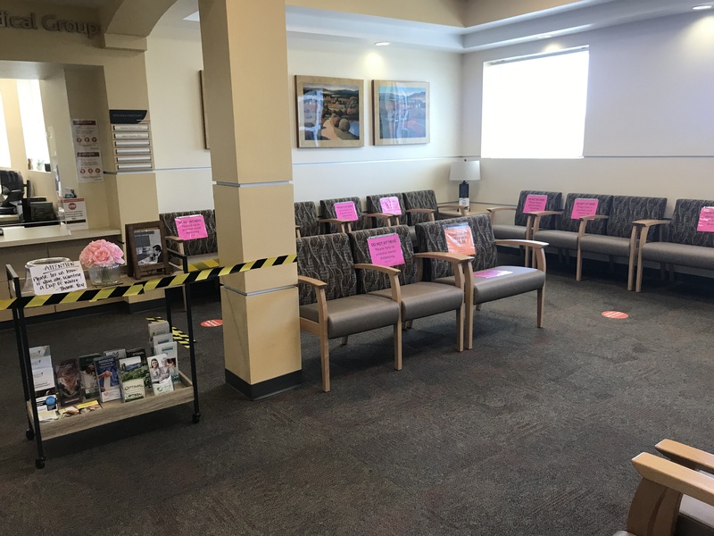 The waiting room at a medical center featuring chairs blocked off with signs saying Do Not Sit Here, Please help us practice social distancing.