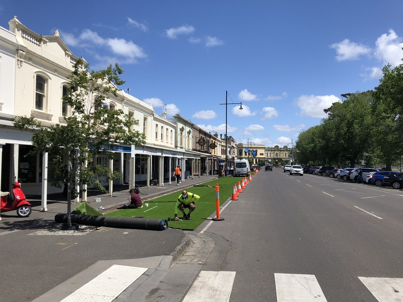 Picture of workers unfurling artificial turf in front of a hospital in Melbourne, Australia.