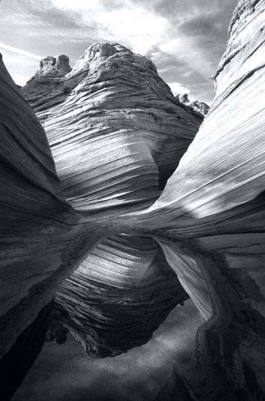 This is a black and white photo of the image of a canyon reflecting from a pool of water at its bottom.