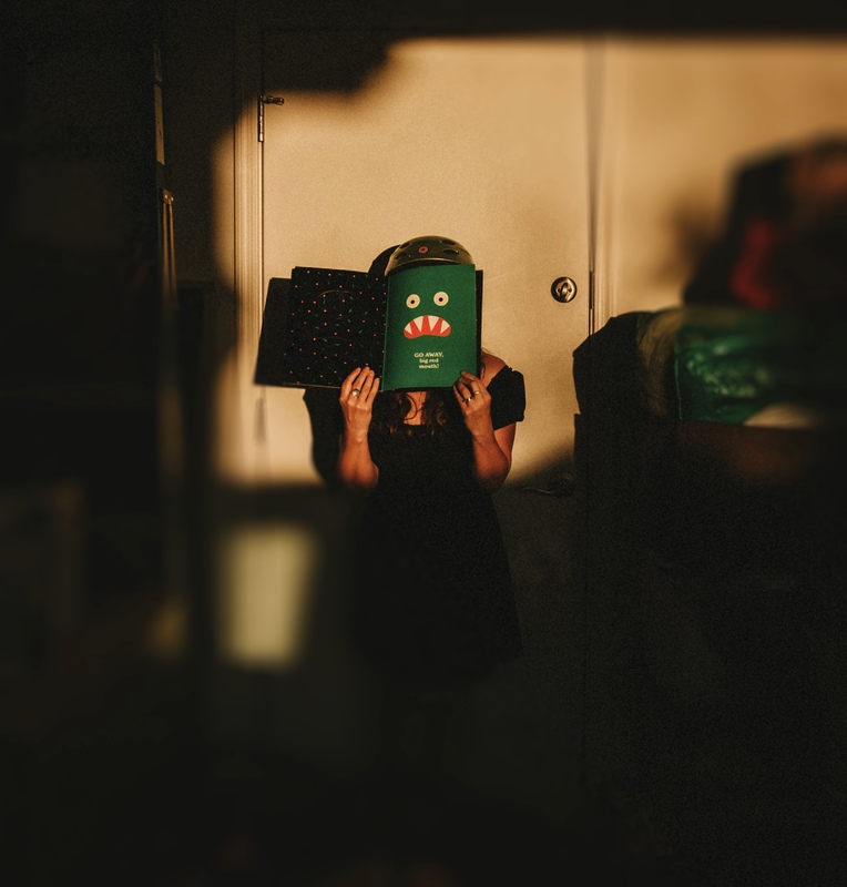 A person is wearing a helmet on their head with a book covering their face and on the book is a monsters face. 