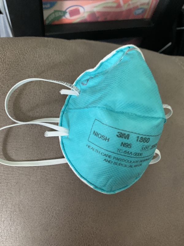 Teal 3M N95 mask laying on a leather piece of furniture. 