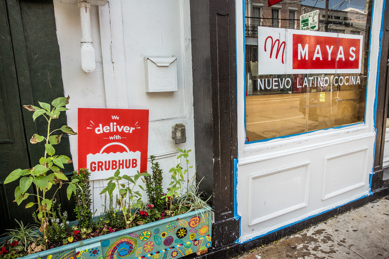 A "We deliver" Grubhub sign next to Mayas Nuevo Latino Cocina in New Orleans.