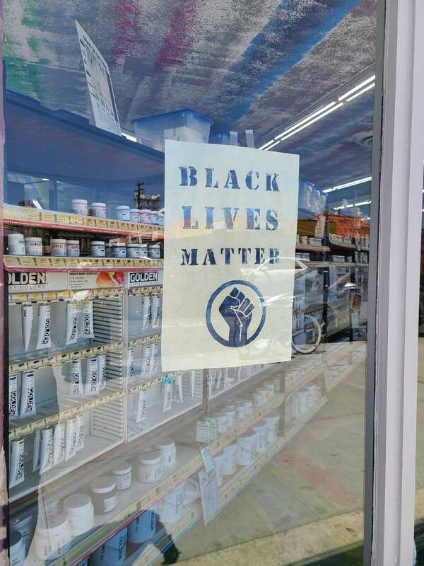 This is a picture of a sign in a storefront window which reads "Black Lives Matter", followed by the Black Power Movement symbol of a raised fist. 