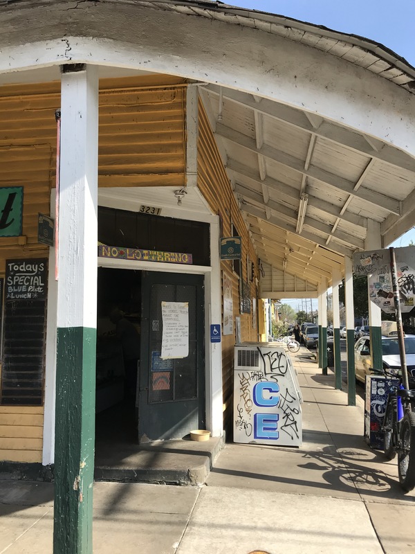 A yellow and white corner store that has its black front door propped open. The right door has a paper sign taped on the front.