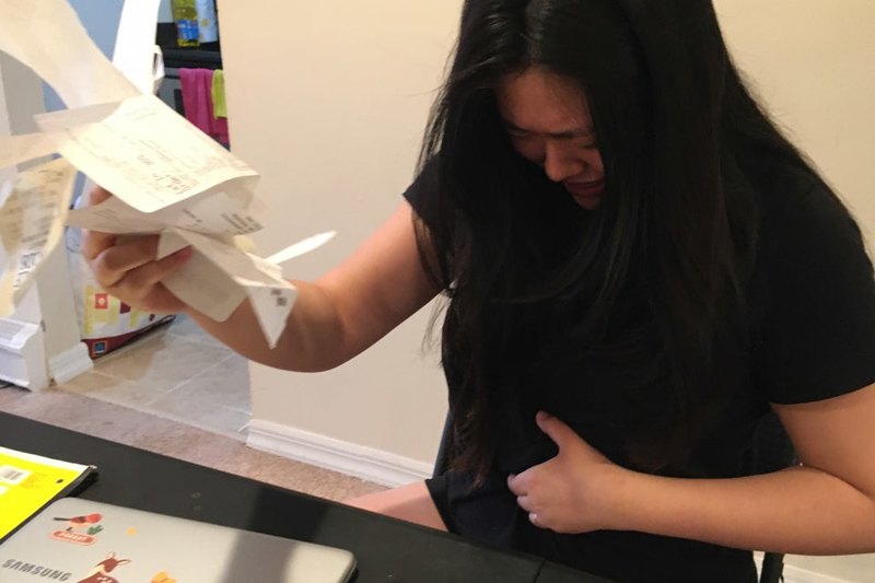 A person is holding receipts in one hand and their stomach in the other.