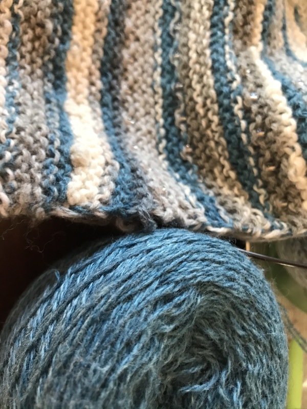 Photo of a blue, white, and gray piece of knitwork next to a ball of blue yarn.