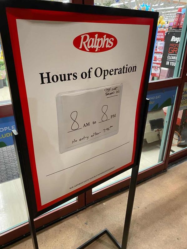 A sign to a grocery store that displays hours of operation.