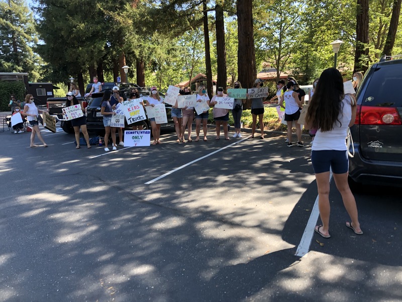 This is a picture taken of a group of people holding signs and protesting in a parking lot.