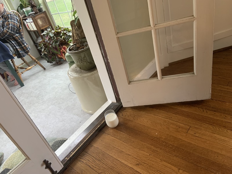 In front of a doorway is a glass of milk placed on the ground.